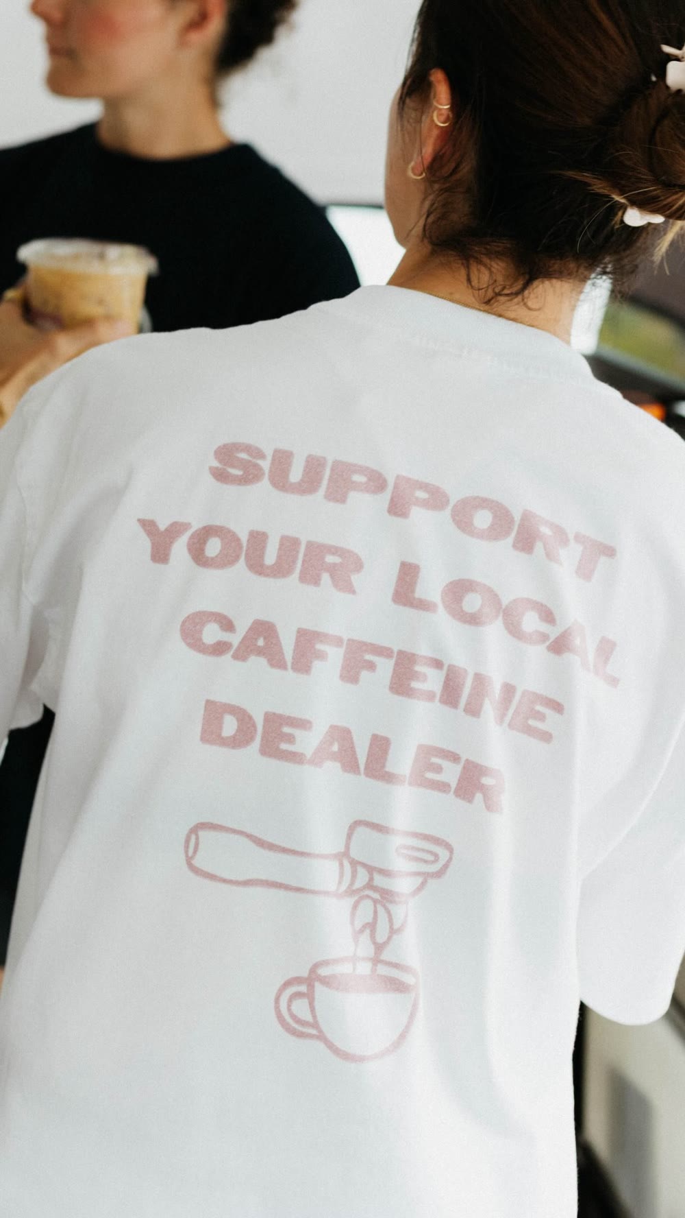 Barista in a Support Your Local Caffeine Dealer tee at the espresso machine