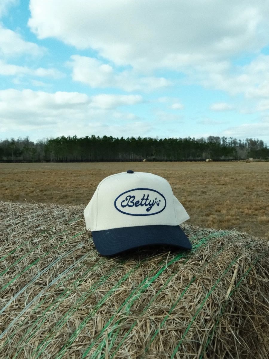 Navy & natural embroidered Betty's logo hat on a hay bale